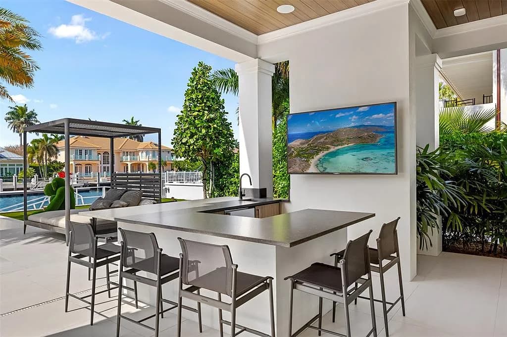 Covered summer kitchen with concrete counter island, bar seating and pool views
