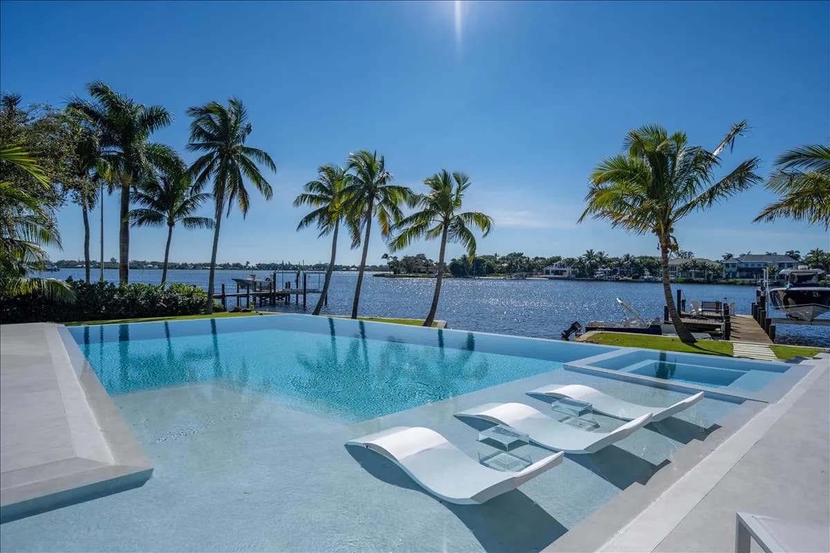 Infinity pool with in-water loungers, palms, and Loxahatchee River views