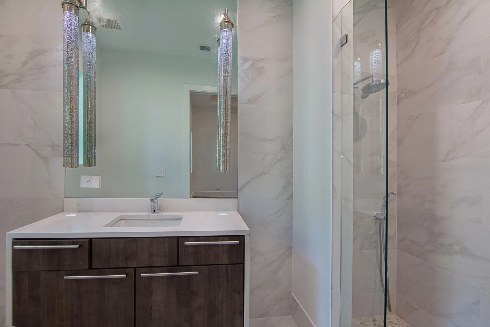 Guest bath with dark wood vanity, marble walls, glass shower, and cylinder pendants