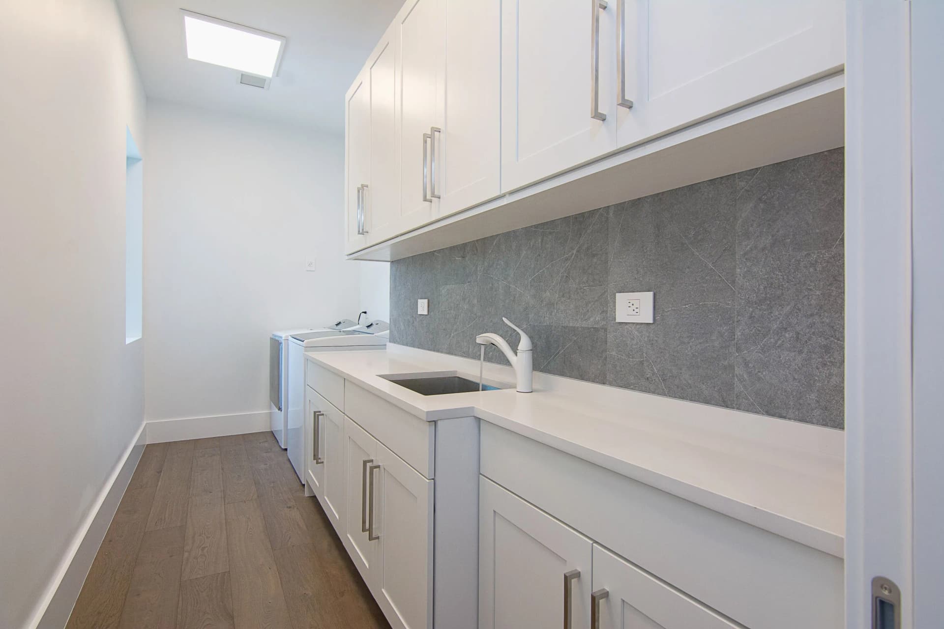 Secondary laundry with white cabinets, gray stone backsplash, and sink
